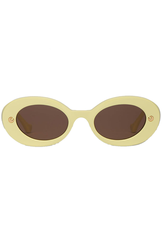 Nanushka oval sunglasses in pale yellow with metal moon signs, shown against a plaid white background.