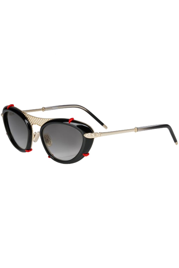 Rotated view of Christian Louboutin cat-eye sunglasses in gray with black frame, red details and metal reticulated temple, shown against a plaid white background.