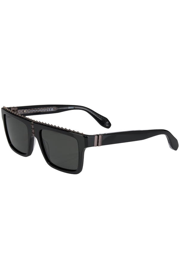 Rotated view of Christian Louboutin sunglasses in gray with black frame and spiny details, shown against a plaid white background.