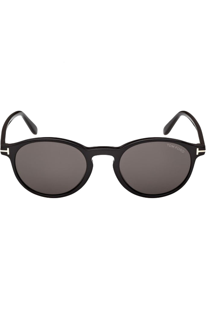 Tom Ford oval sunglasses in gray with black frame and metal T details, shown against a plaid white background.