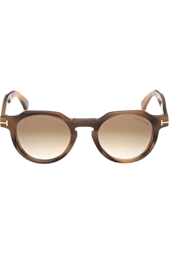 Tom Ford oval sunglasses in brown with tortoise frame and gold T details, shown against a plaid white background.