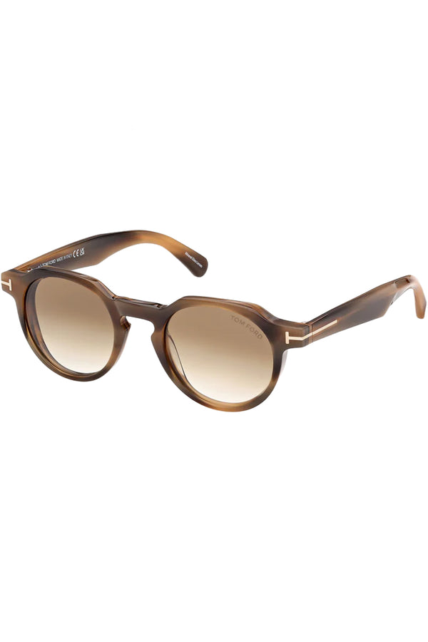 Rotated view of Tom Ford oval sunglasses in brown with tortoise frame and gold T details, shown against a plaid white background.