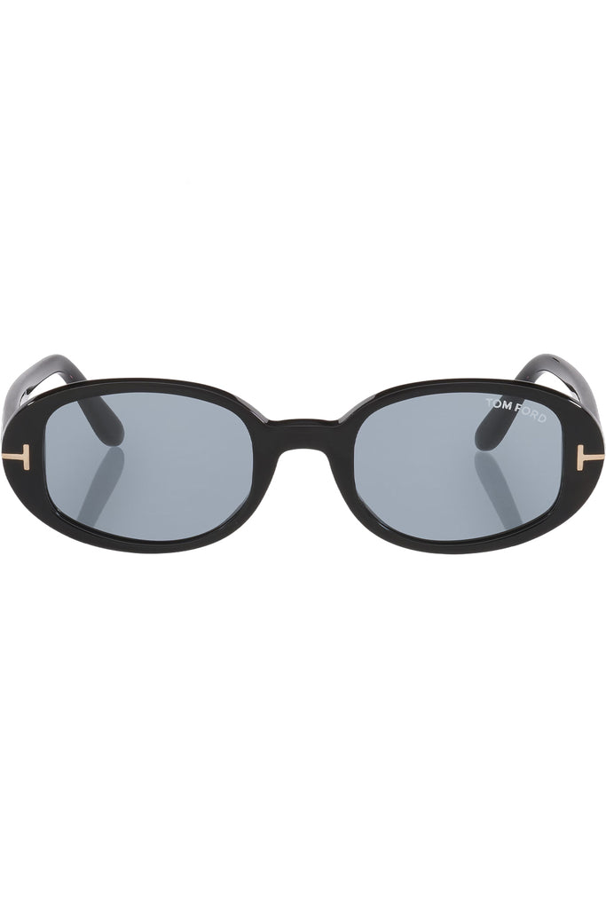 Tom Ford oval sunglasses in blue with black frame and gold T details, shown against a plaid white background.