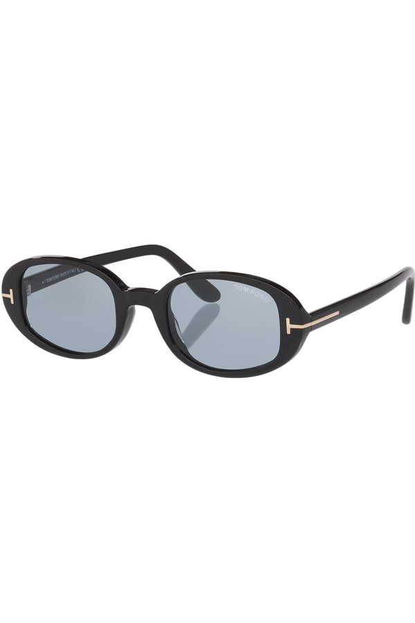 Rotated view of Tom Ford oval sunglasses in blue with black frame and gold T details, shown against a plaid white background.