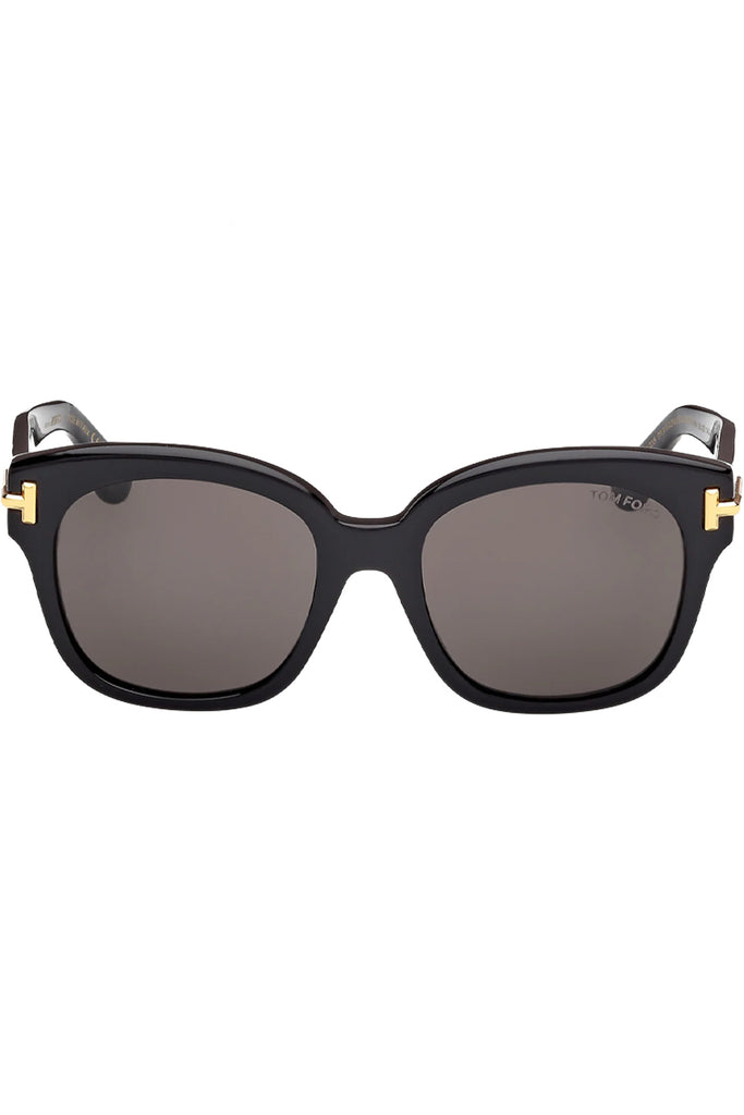 Tom Ford oval sunglasses in gray with black frame and gold T details, shown against a plaid white background.