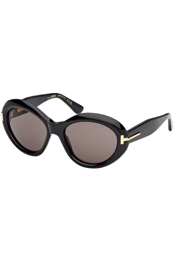Rotated view of Tom Ford oval sunglasses in gray with black frame and gold T details, shown against a plaid white background.