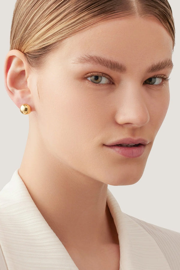 Model wearing the Aurora stud earrings in gold colour from the brand JENNY BIRD